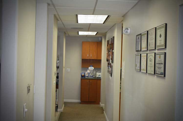 A hallway of a dentist office with walls and brown cabinets, Framed certificated hanged on the wall