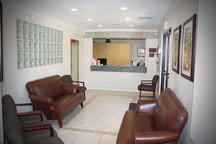 A reception area with white walls, framed photos on the wall, brown couches, light brown cabinets