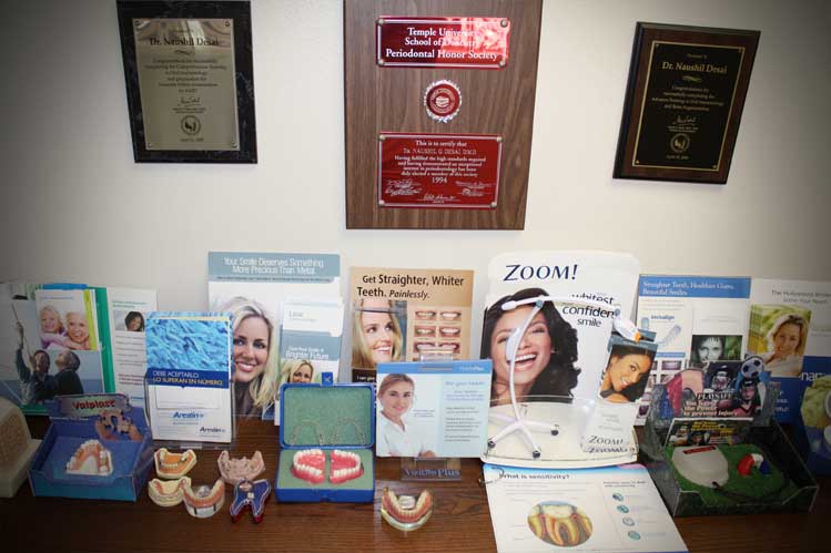 3 awards displayed on a wall, different dental flyers on a table and some teeth models displayed on a table