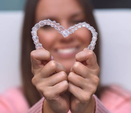 Woman smiling in the background holding and made a heart shape with incasalign